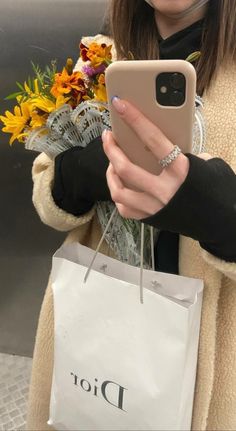 a woman holding a phone in her right hand while wearing a fur coat and carrying a bouquet of flowers