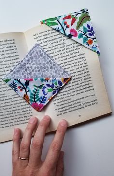 an open book with some fabric on it and a person's hand next to it