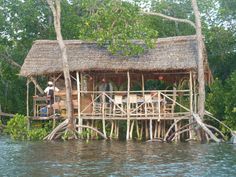 a hut built on stilts in the middle of water with people standing outside it