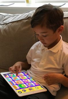 a little boy sitting on a couch playing with an ipad