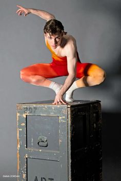 a man in red and orange is standing on top of an old filing cabinet with his arms outstretched