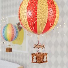 two hot air balloons in the shape of a basket hanging from a ceiling with string lights