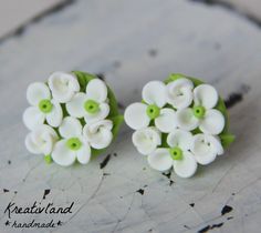 two green and white flower earrings sitting on top of a piece of wood with holes in the middle