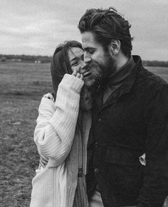 a man and woman standing next to each other in a field, one is kissing the other's forehead