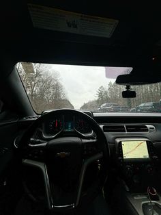 the interior of a car with dash lights on and dashboard screen showing, in front of trees