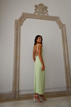 a woman standing in front of a white wall wearing a green dress and high heels