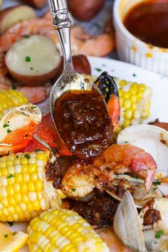 a spoon with some food on top of it next to corn and other foods in the background