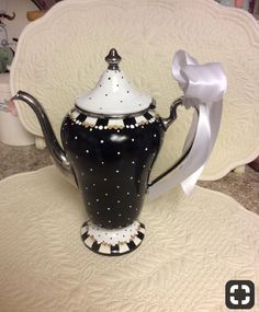 a black and white tea pot with a bow on the top sitting on a table