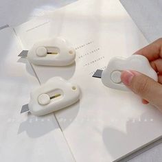 a hand is holding two white staplers on top of a piece of paper