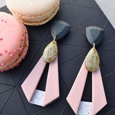 two pink and gold earrings sitting next to a cupcake