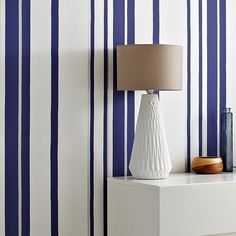 a white vase sitting on top of a table next to a blue and white striped wall