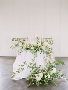 a table with white flowers and greenery is set up in front of a wall