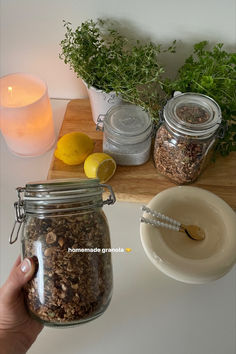 a person holding a jar filled with granola next to some lemons and herbs