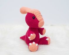 a pink crocheted stuffed animal sitting on top of a white bedding sheet