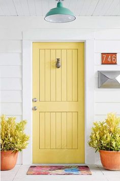 a yellow door with two potted plants in front of it and a mailbox on the wall