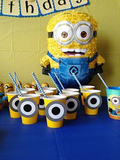 a table topped with cups filled with yellow frosted drinks and minion birthday decorations