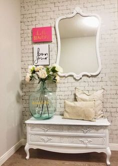 a vase with flowers sitting on top of a white dresser next to a brick wall