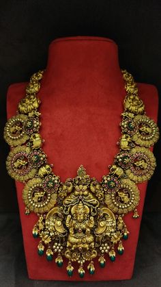 an elaborate necklace is displayed on a red velvet stand with gold jewelry and green beads