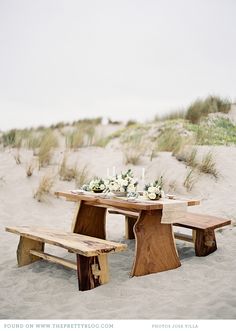 a wooden table and bench on the beach with flowers in vases sitting on it