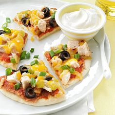 four slices of pizza on a white plate with olives, cheese and sour cream