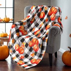 a plaid blanket with pumpkins on it sitting in front of a chair and table