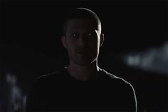 a man standing in the dark with his head turned to the side and looking at the camera