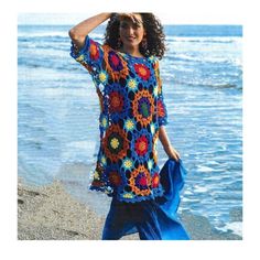 a woman standing on top of a beach next to the ocean wearing a colorful crocheted dress