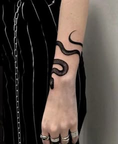 a person with a snake tattoo on their arm holding onto a chain and wearing rings