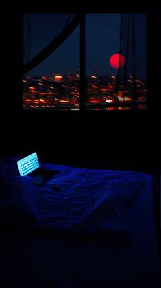 a laptop computer sitting on top of a bed in a dark room next to a window