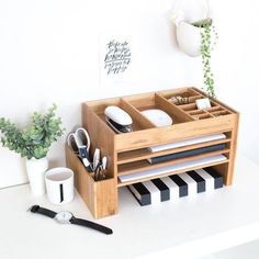 a wooden drawer with utensils and plates in it next to a potted plant