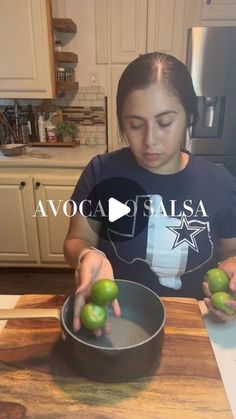 a woman is holding two green apples in a pan on a kitchen counter with the words avocado salsa above her