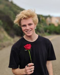 a young man with blonde hair holding a red rose