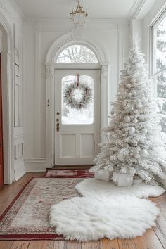 a white christmas tree sitting in front of a doorway with a wreath on it's door