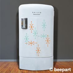 a white refrigerator sitting on top of a hard wood floor next to a gray wall