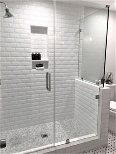 a bathroom with a walk in shower next to a white toilet and black and white tile floor