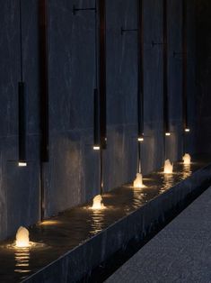 several lights are lit up on the side of a wall by water in a fountain