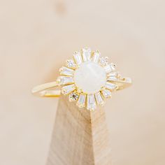 a diamond and gold ring on top of a wooden stand with a white stone in the center