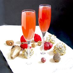 two champagne flutes with raspberries, pineapples and other holiday decorations on a napkin