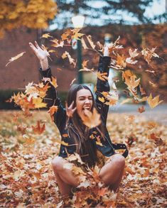 a woman is sitting in the leaves with her hands up