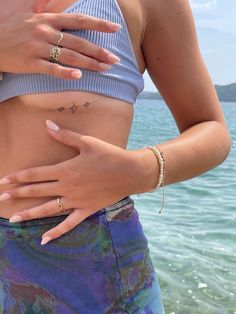 a woman standing in front of the ocean with her hands on her hip and wearing rings