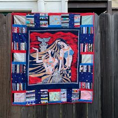 a quilt hanging on a wooden fence next to a building