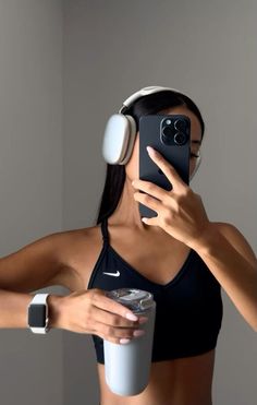 a woman wearing headphones is holding a cup and looking at her cell phone while taking a selfie