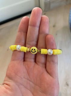 a hand holding a yellow beaded bracelet with smiley face on it's end