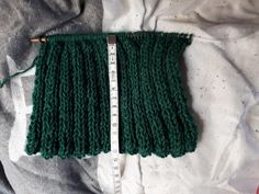 a piece of green knitted material with a measuring tape in front of it on a bed