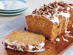 a loaf of carrot bread with white frosting and pecans on top, sitting on a cutting board