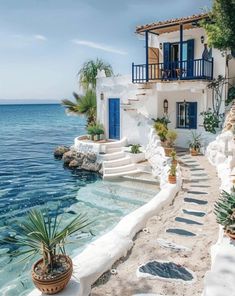 a white house with blue shutters next to the ocean and stairs leading up to it