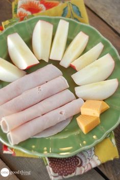 several pieces of meat, cheese and apples on a green plate