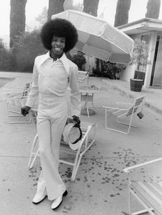 a man with an afro standing in front of some lawn chairs and holding an umbrella