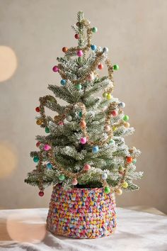 a small white christmas tree in a pot with multicolored ornaments on it's branches