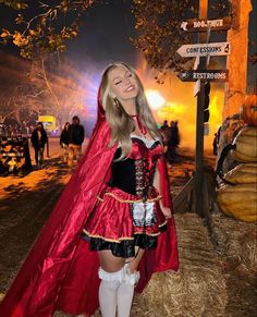 a woman dressed as a red riding hood and cape standing in front of a street sign